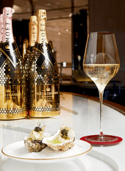 A glass of champagne sits next to a plate of oysters in the bar