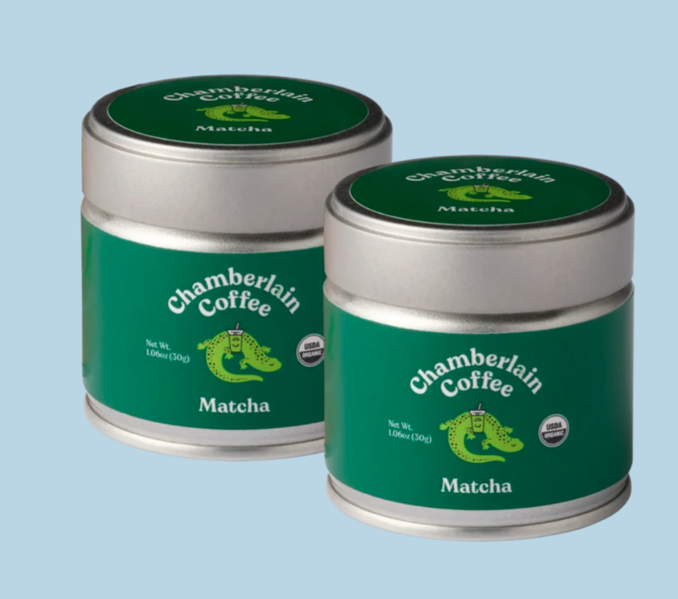 Two green matcha tins sit next to each other against baby blue backdrop. 