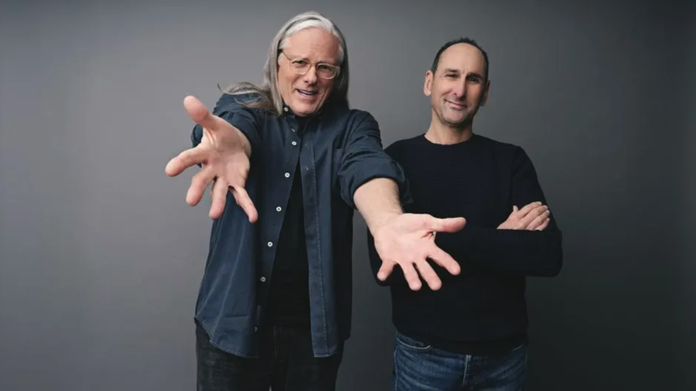 Jeff Goodby and Rich Silverstein stand in front of a grey background with playful smiles on their faces. 