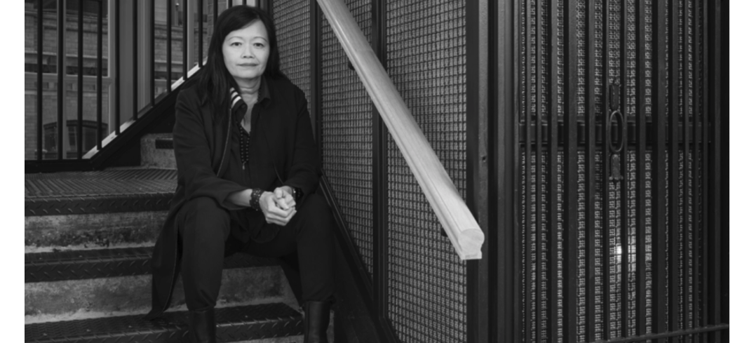 Judy John sits on a metal staircase looking directly into the camera. 
