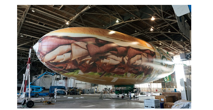 A blimp in a warehouse that looks like a giant sub sandwich