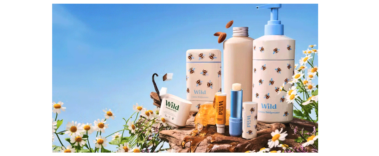 Wild deodorant and other cosmetics sit near honey and daisies against a blue sky.  